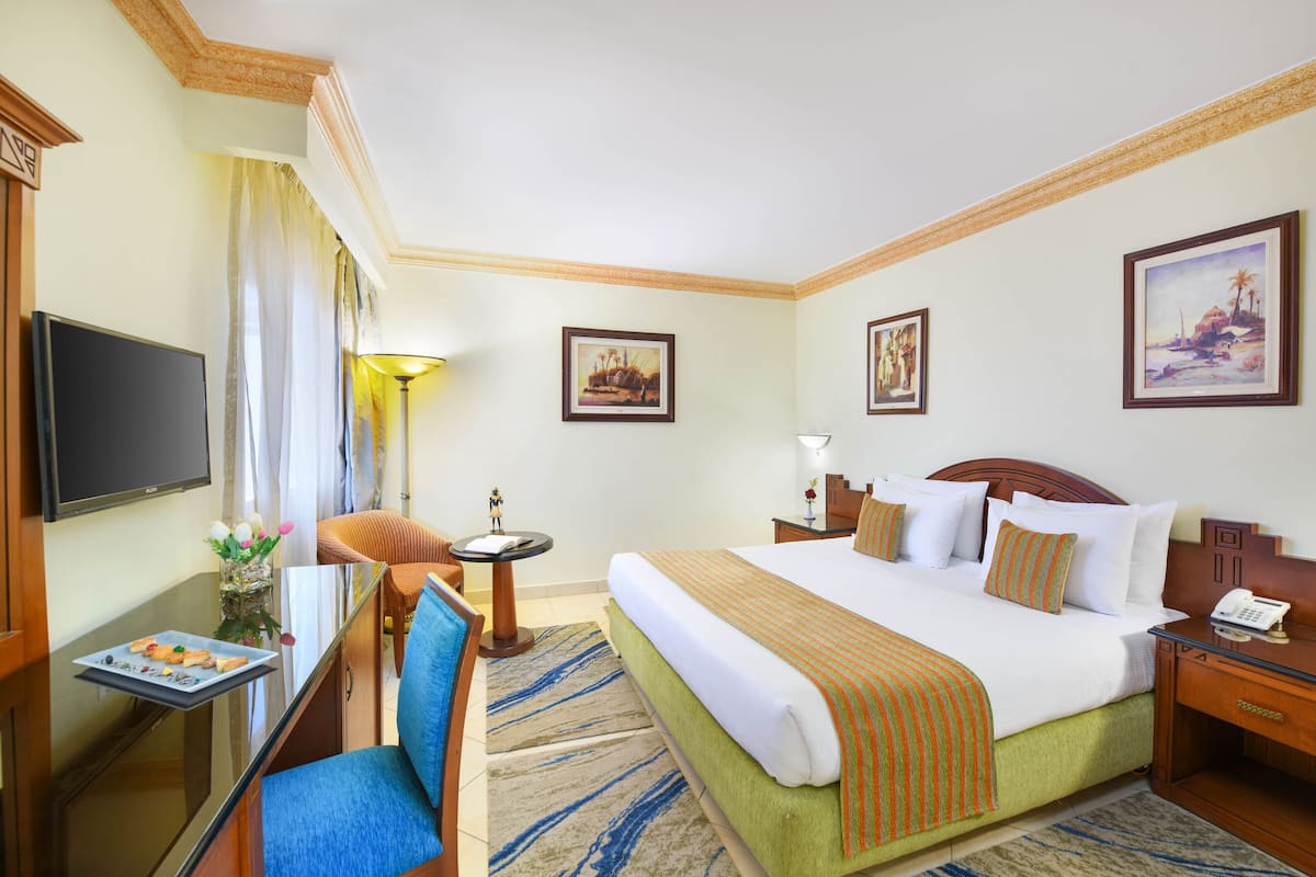 Une chambre d’hôtel comprenant un lit, un bureau avec une chaise, une télévision et des œuvres d’art encadrées accrochées aux murs.