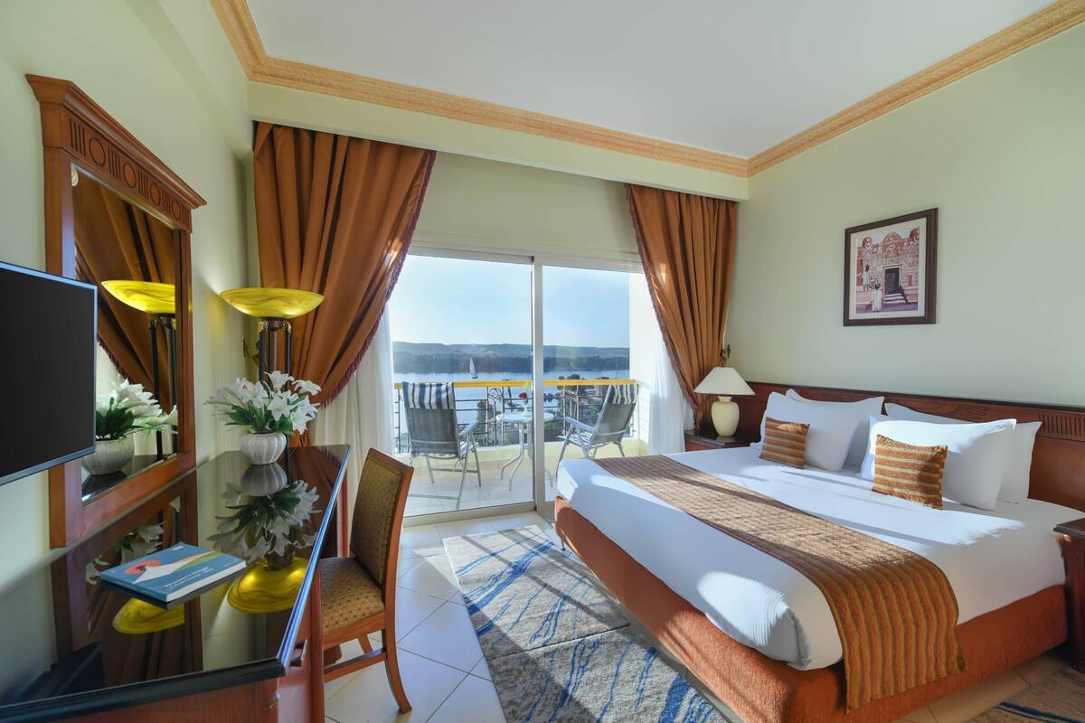 Une chambre d’hôtel avec un lit, un bureau avec un ordinateur, une chaise, une télévision et un balcon avec vue.