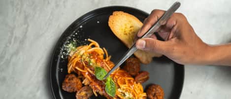 A black plate with spaghetti, meatballs, and a piece of bread on a marble surface.