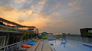 A rooftop pool area with a view of the sunset, a small colorful playhouse, and a covered seating area with colorful cushions. - Grand Tjokro Premier Bandung (Bandung)