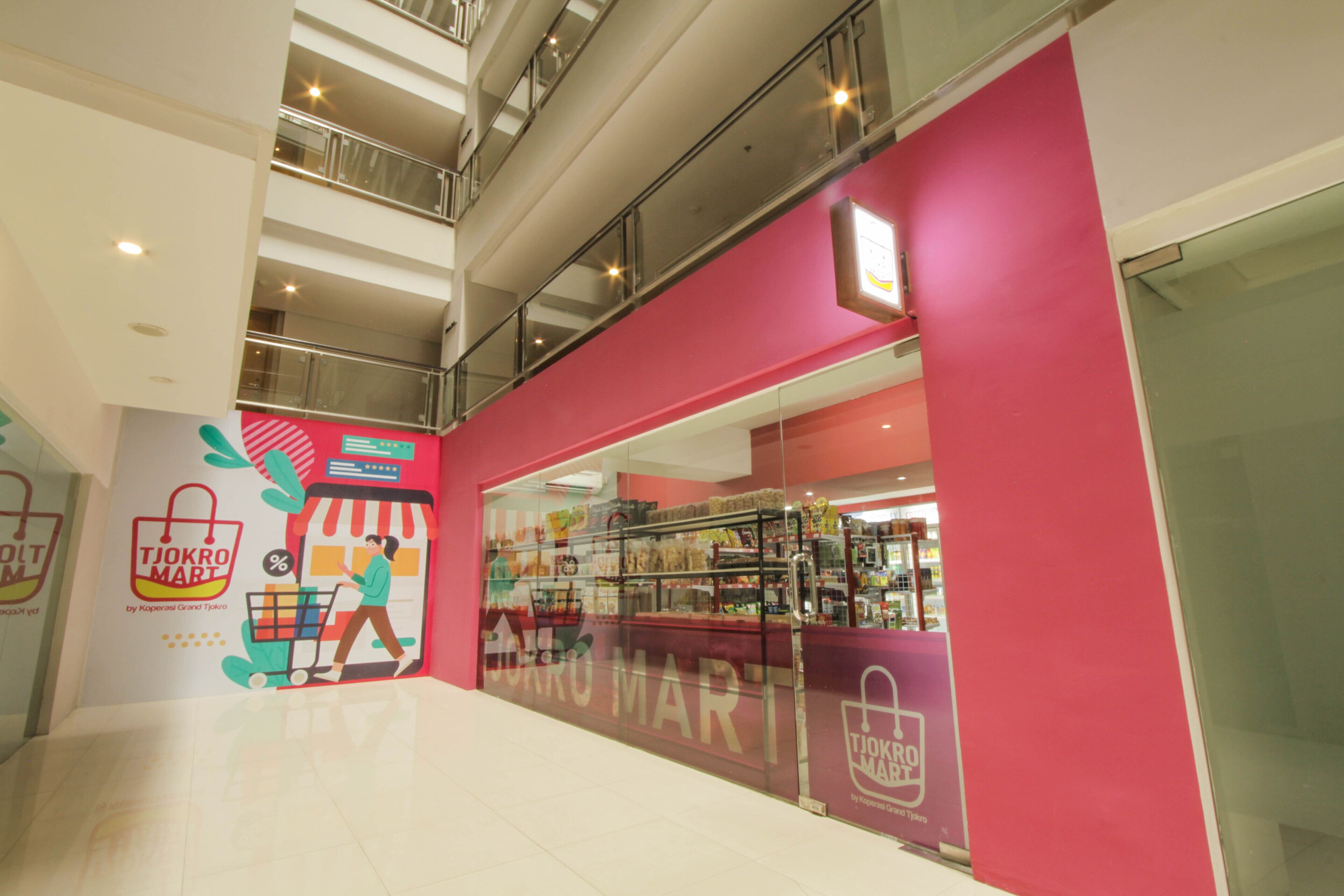 A shopping mall interior with a TJOKRO MART store featuring a bright pink facade and a glass entrance.