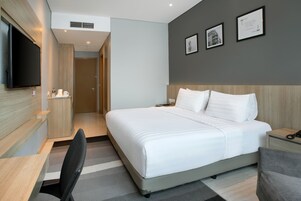 Hotelkamer met een groot bed, een bureau, een stoel, een flatscreen-tv en een muur met ingekaderde foto's.