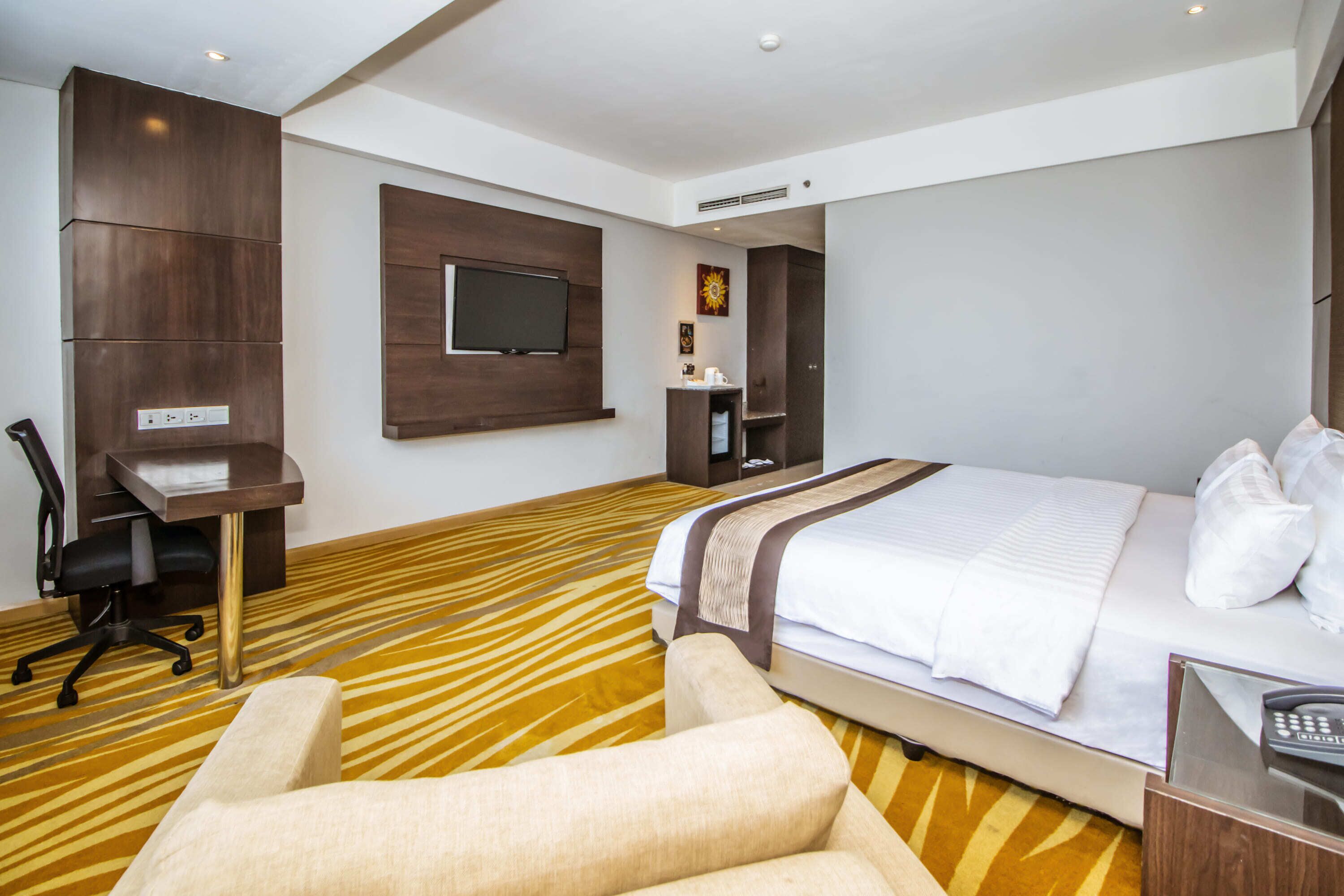 Quarto de hotel com cama, escrivaninha, cadeira, televisão e banheiro.