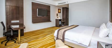 Quarto de hotel com cama, escrivaninha, cadeira, televisão e banheiro.