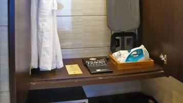 A compact bathroom with a towel rack, an ironing board, a shoe rack, and a small electronic device on a shelf.