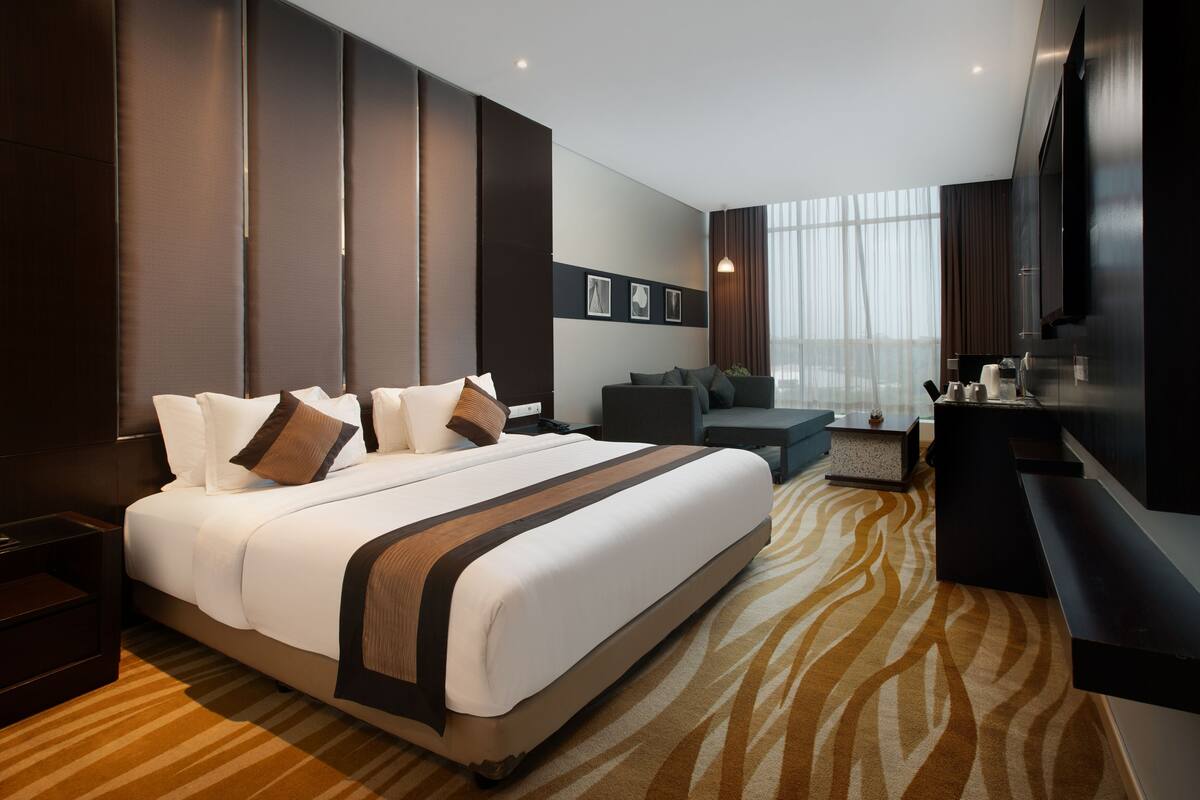 A modern hotel room with a large bed, a sofa, a desk, and a TV.