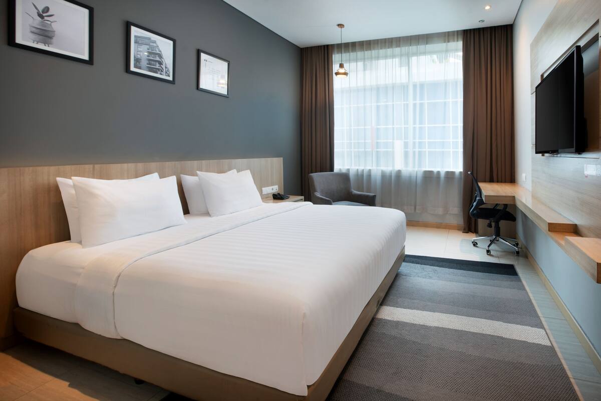 A hotel room with a large bed, a desk, a chair, and a TV.