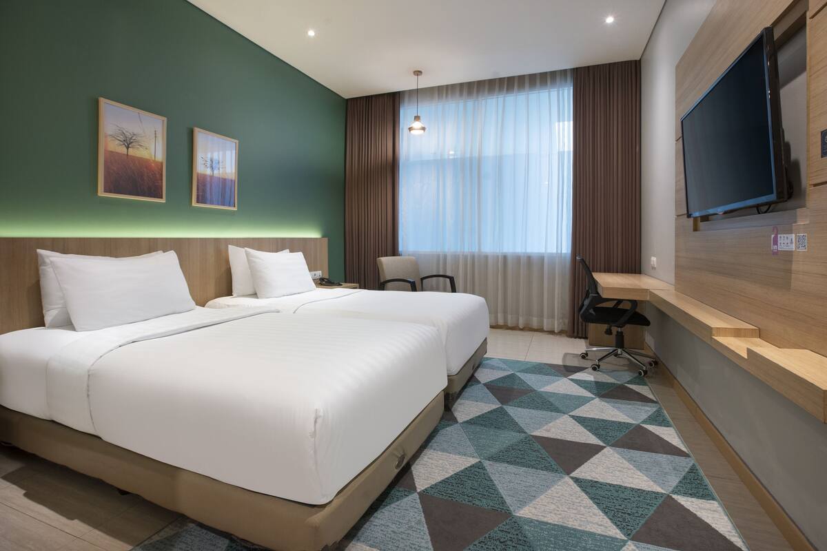 A hotel room with a large bed, a desk, a chair, a TV, and artwork on the wall.