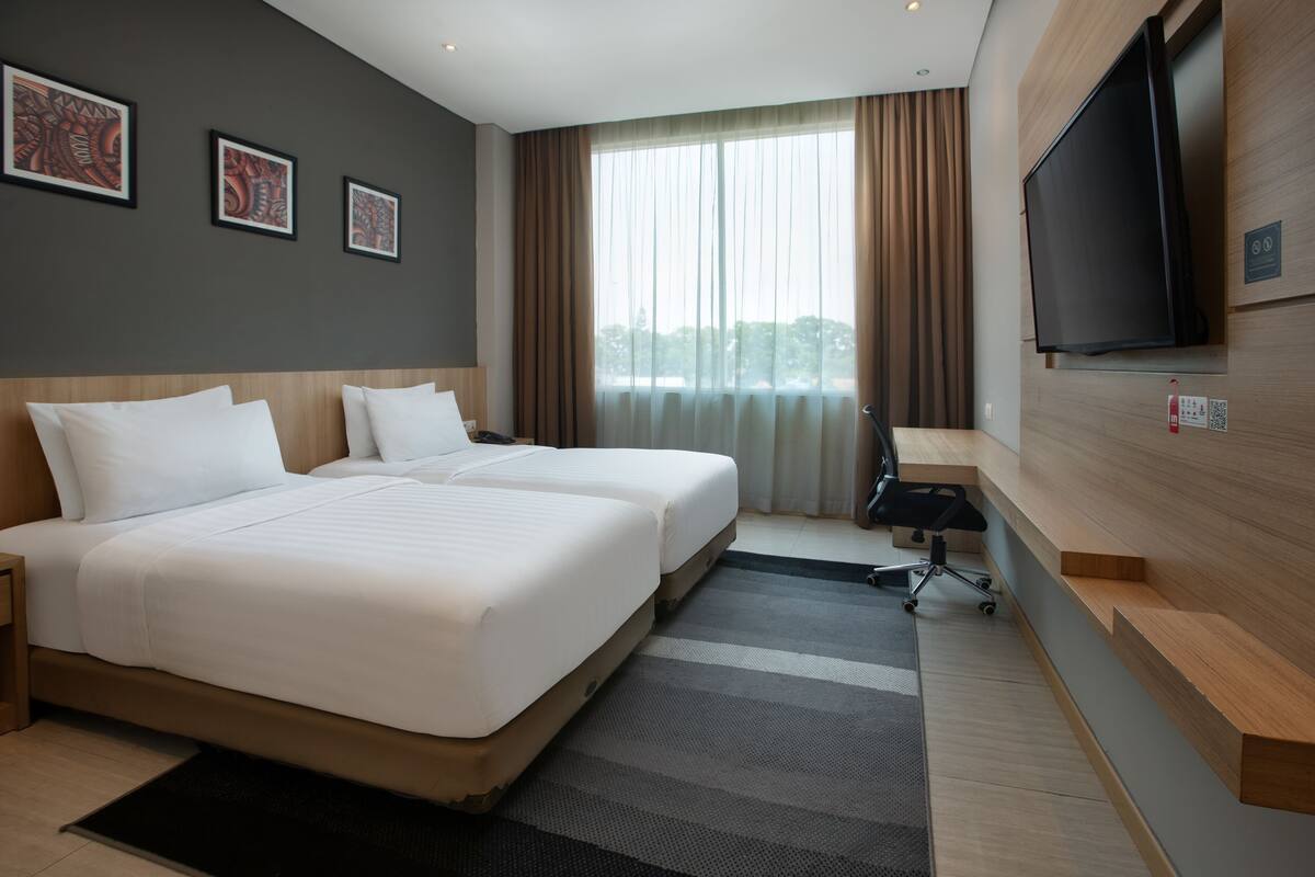 A hotel room with two beds, a desk, a chair, a TV, and a window with curtains.
