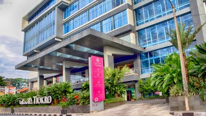 A modern hotel with a prominent sign for Grand Tjokro, featuring multiple floors, large windows, and lush greenery around the entrance. - Grand Tjokro Premier Bandung (Bandung)