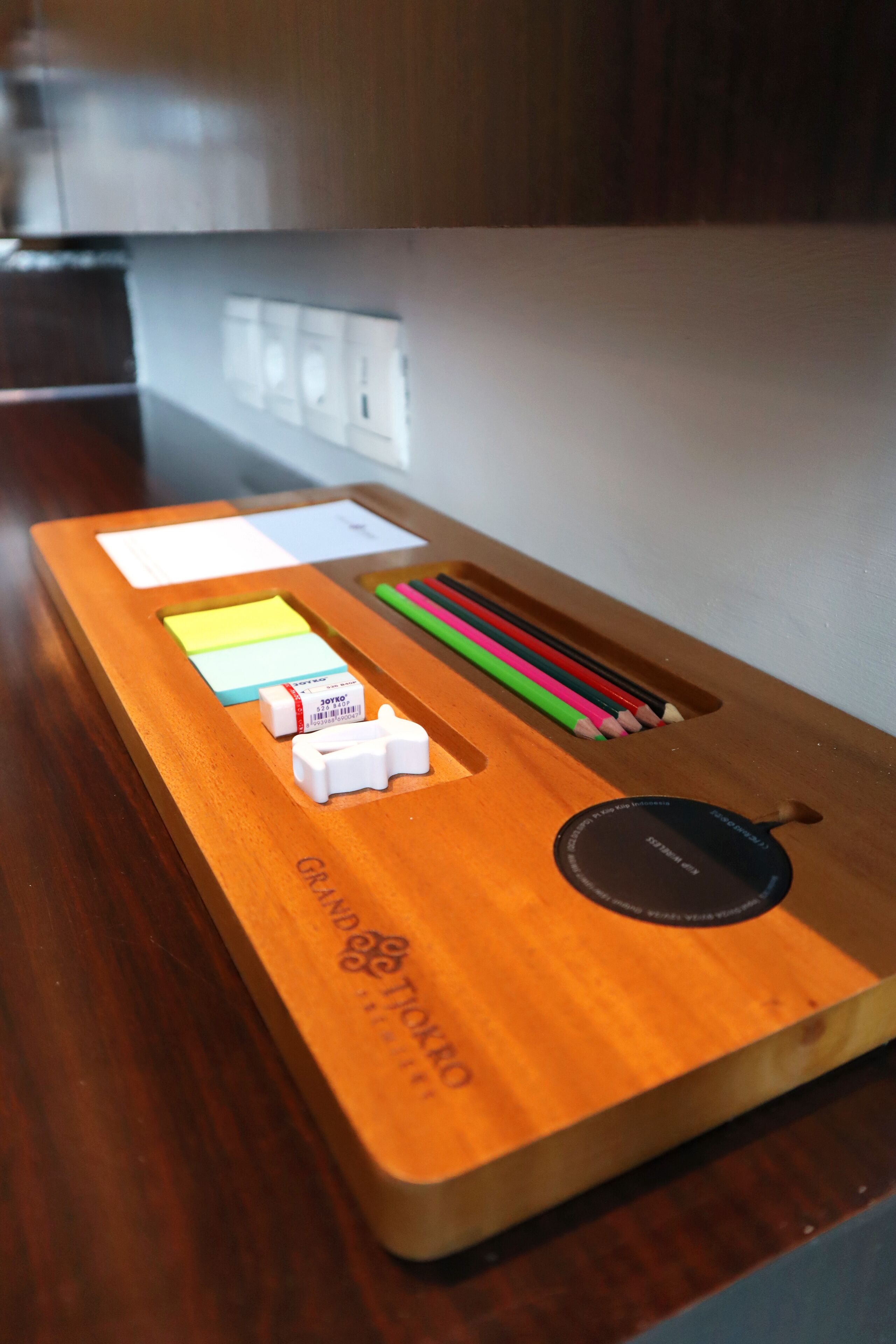 A wooden desk with a corkboard, sticky notes, colored pencils, and a small white object.