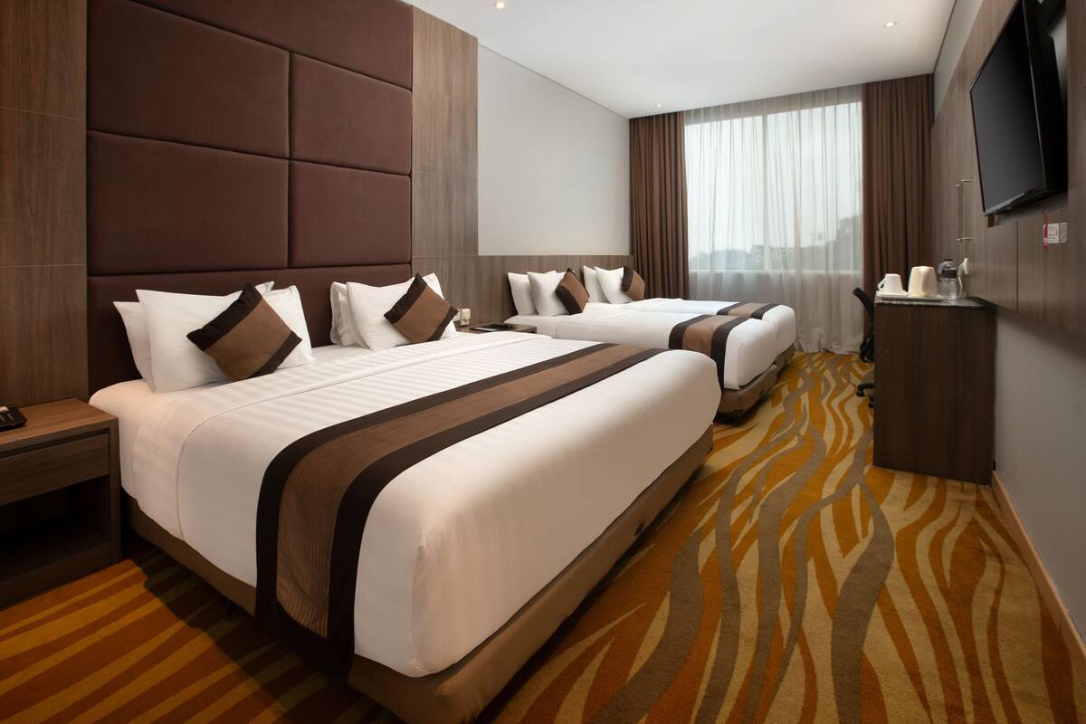 A hotel room with two beds, a flat-screen TV, a minibar, and a large window with curtains.