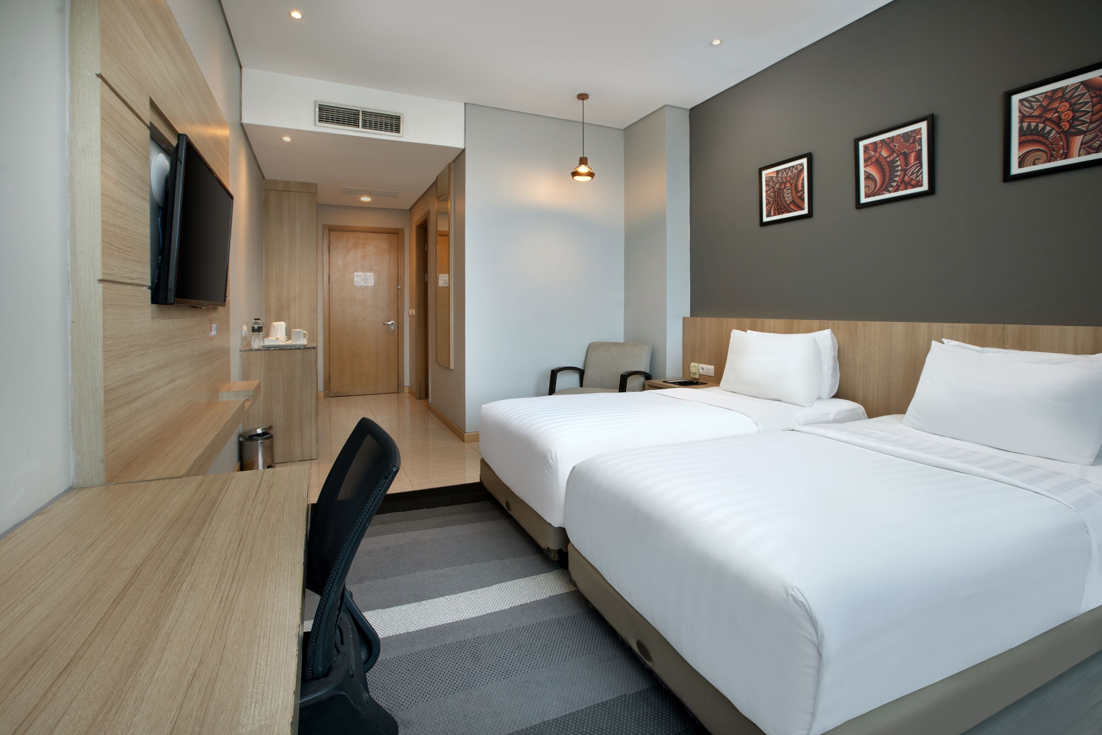 Une chambre d’hôtel avec deux lits, un bureau, une chaise, une télévision et des œuvres d’art accrochées au mur.