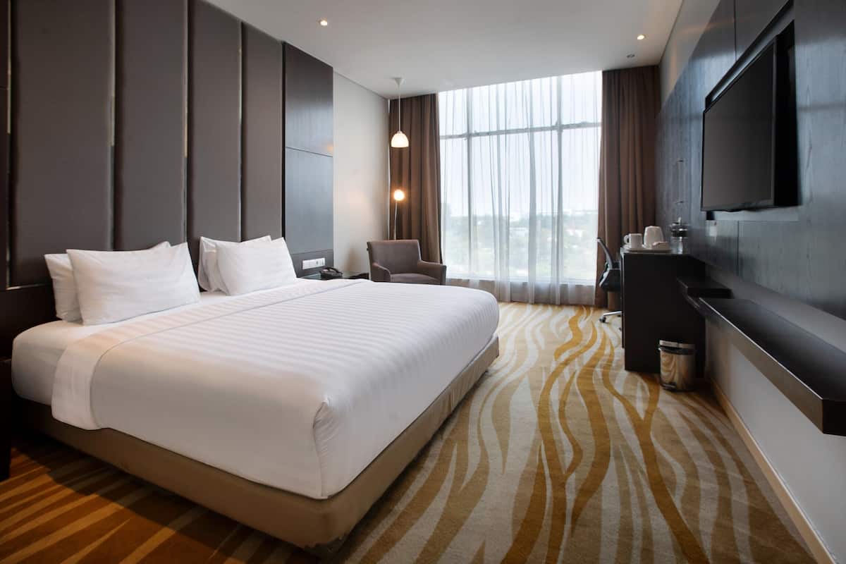 A modern hotel room with a large bed, a flat-screen TV, a desk with a chair, and a large window with curtains.