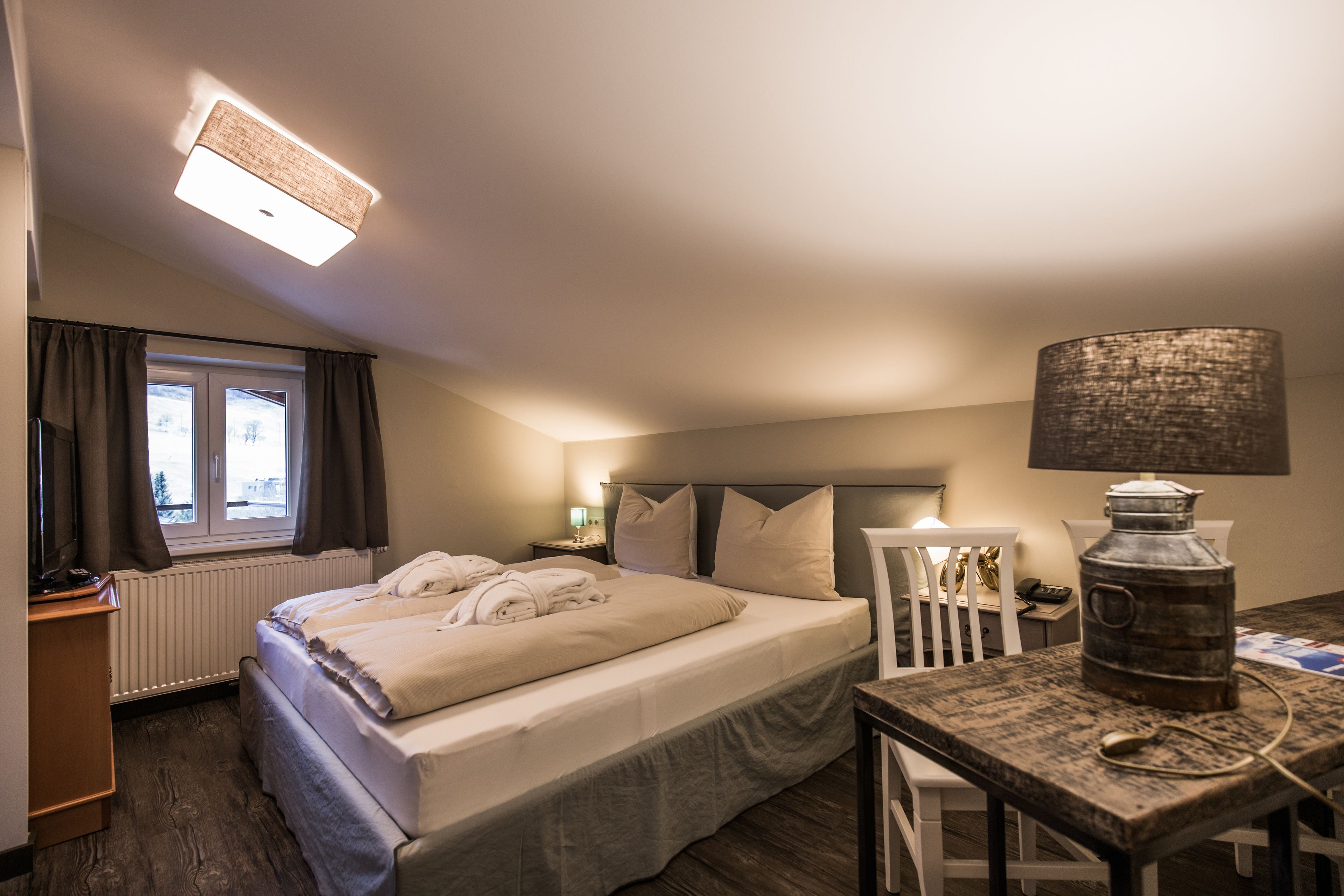 Hotellihuone, jossa on sänky, työpöytä, lamppu ja patteri.