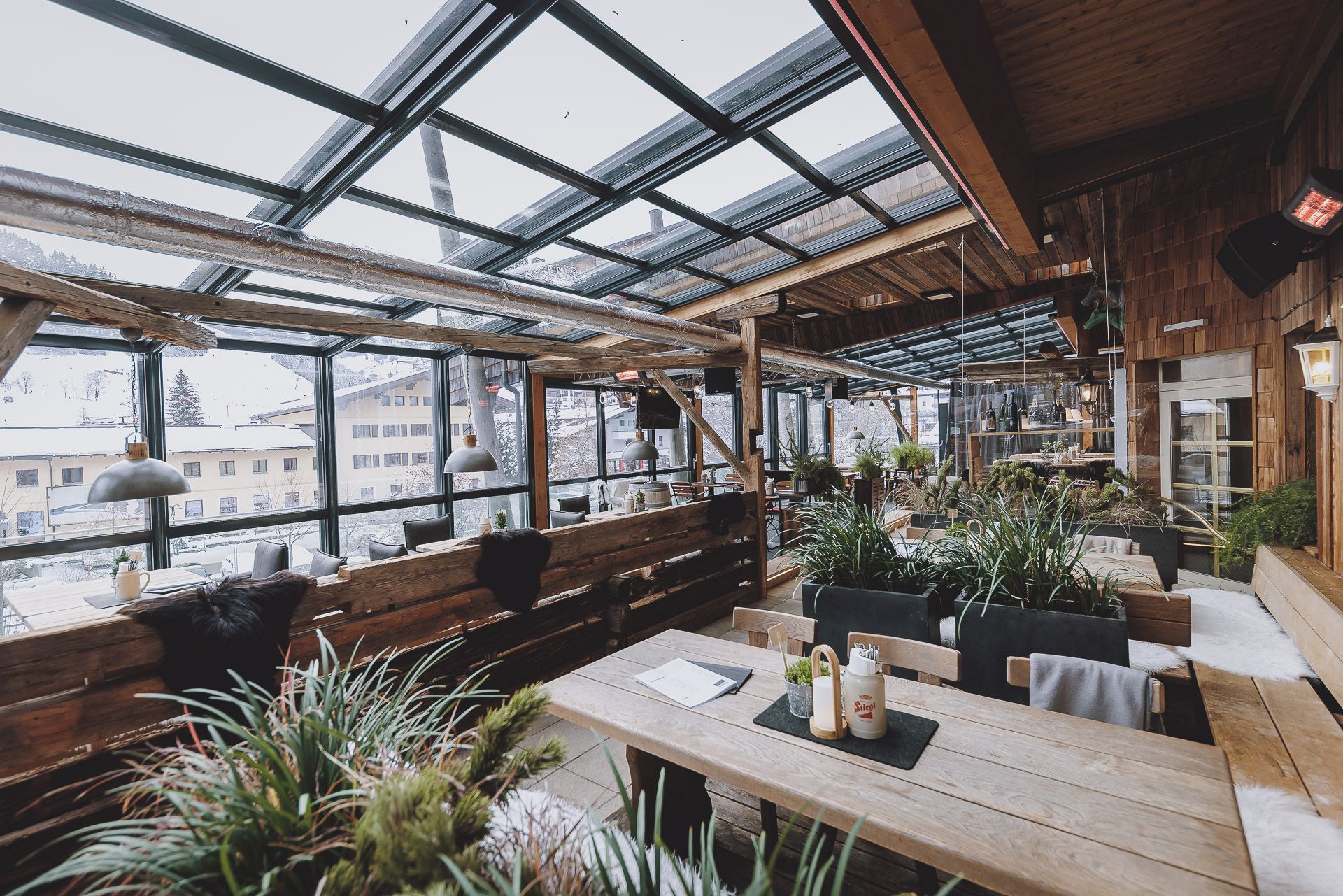 A cozy restaurant with wooden interiors, large windows, and indoor plants.