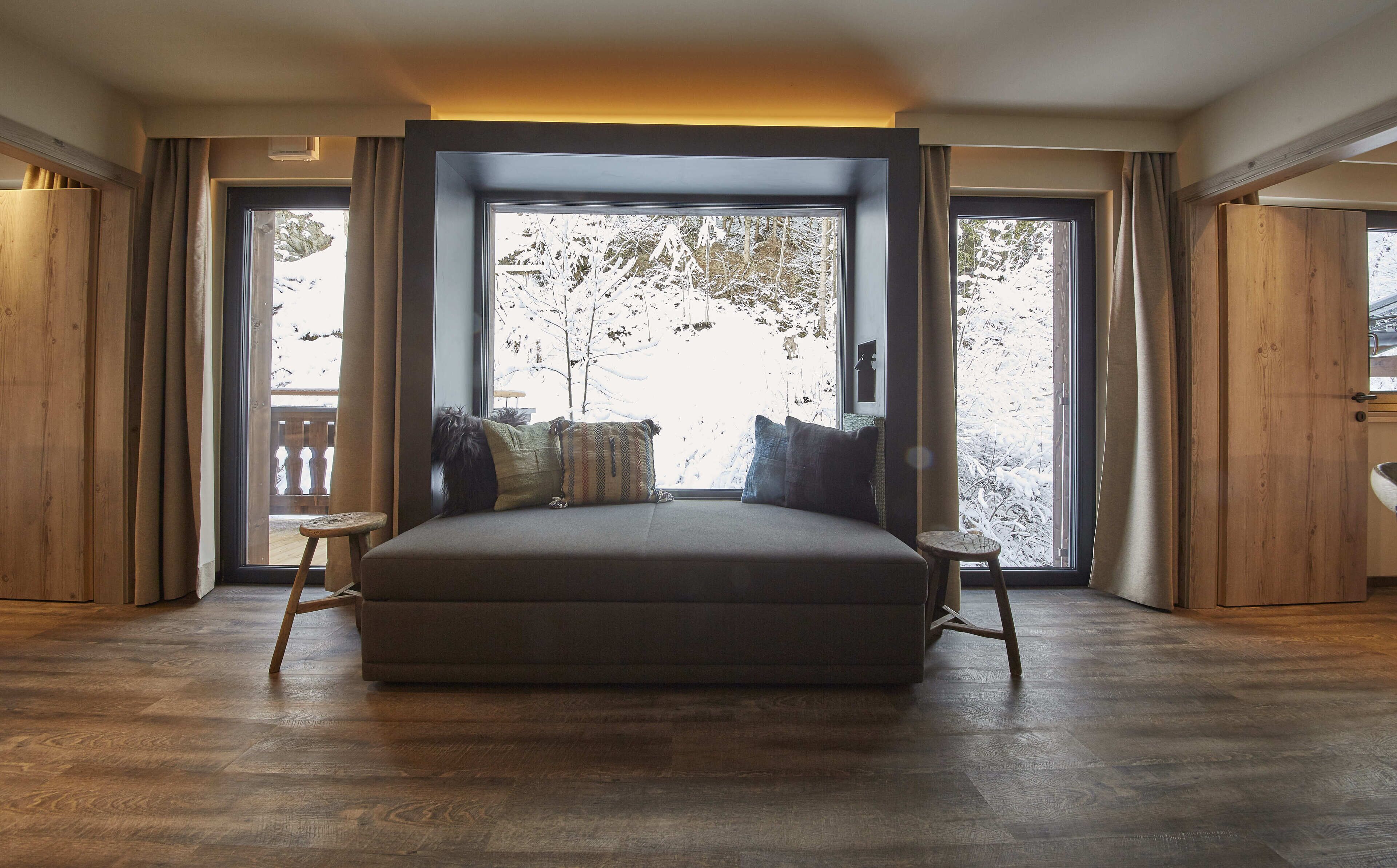 Een slaapkamer met een groot bed, een klein nachtkastje en zicht op een besneeuwd landschap door grote ramen.