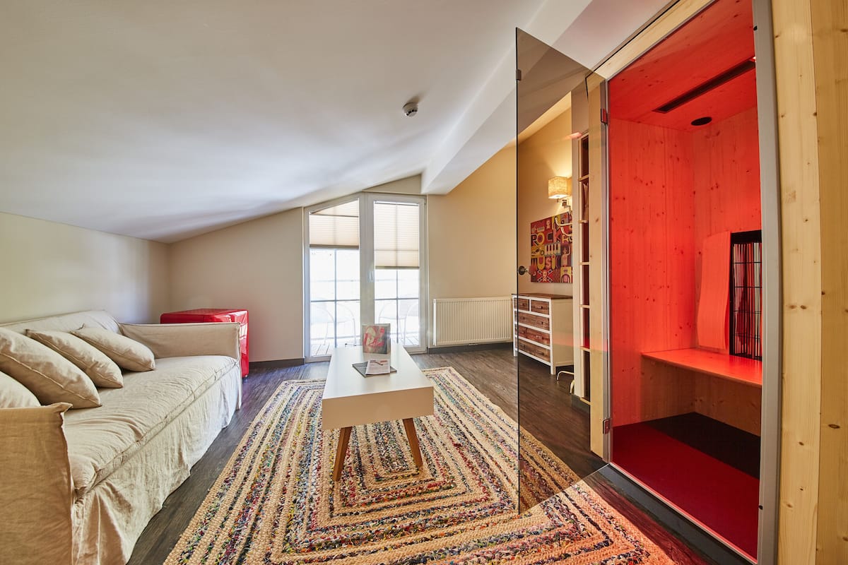 Een moderne woonkamer met een bank, een salontafel en een rode accentstoel. Een groot raam zorgt voor natuurlijk licht en uitzicht op het landschap.