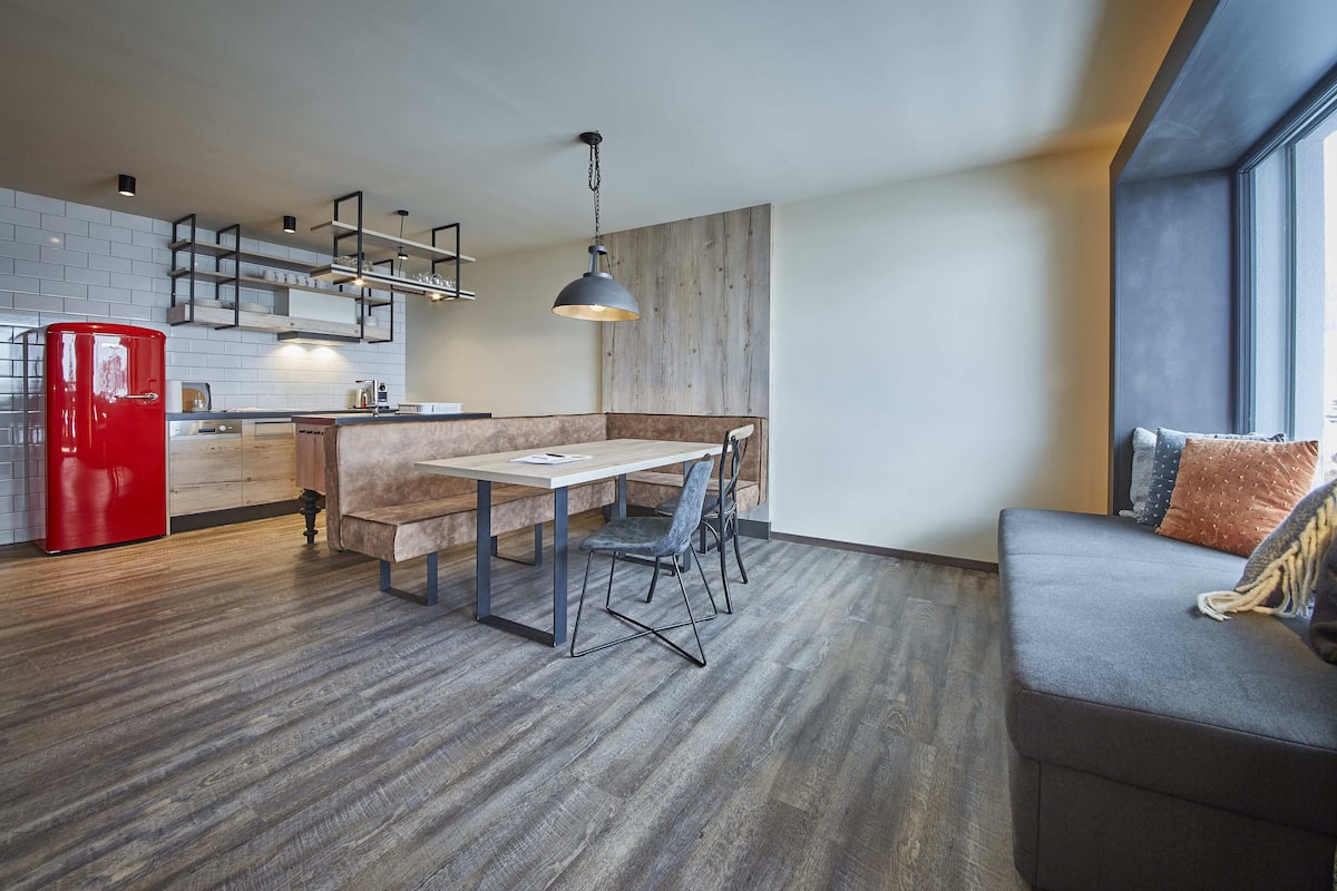 Een moderne keuken met een rode koelkast, houten kastjes en een ingebouwde bank.