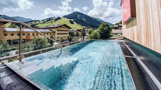 Una piscina con agua cristalina, rodeada de edificios y un paisaje montañoso.