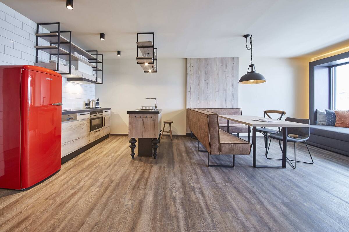 Een moderne keuken met een rode koelkast, houten vloeren en een inbouwwerkbank bij de eettafel.
