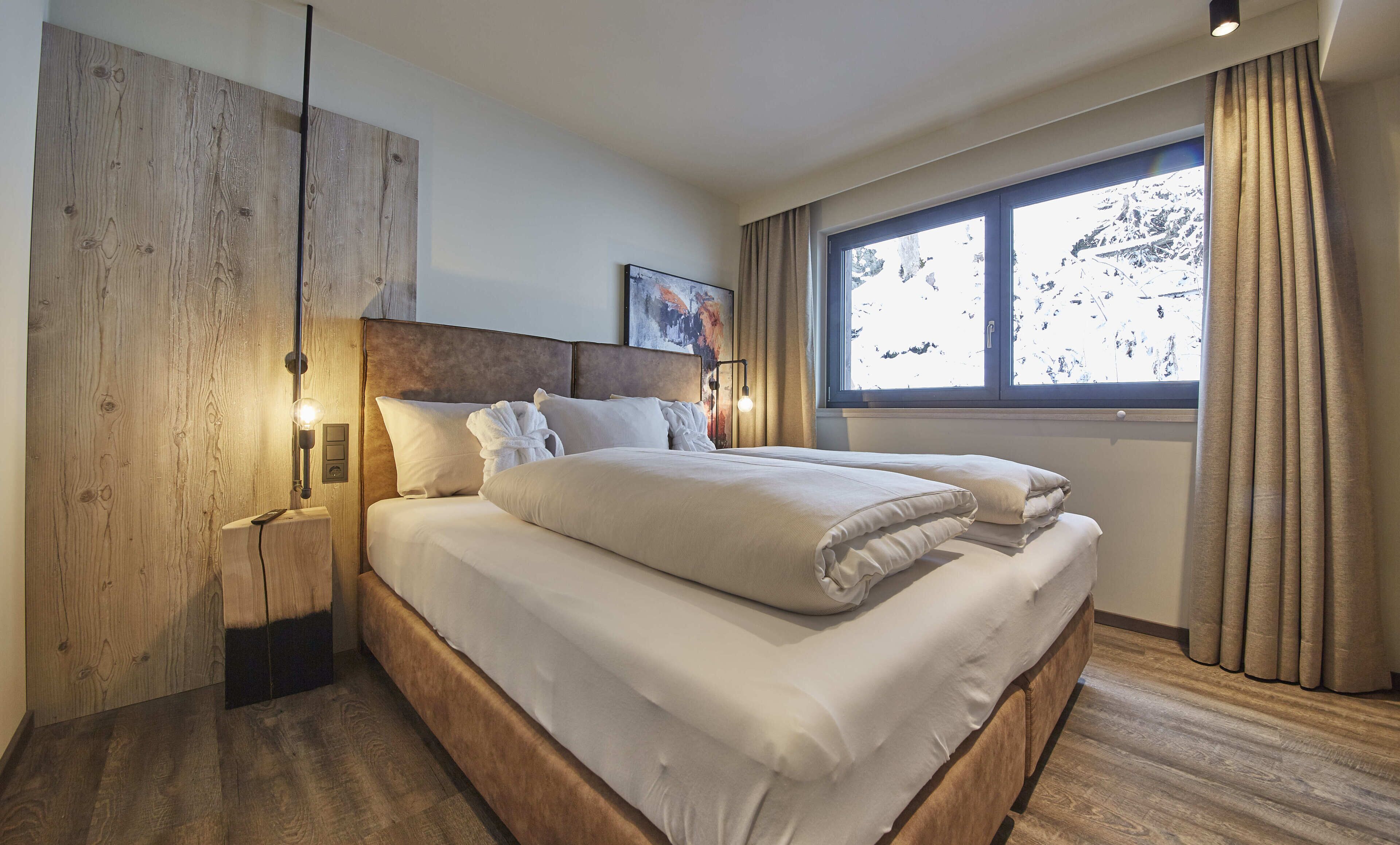 A modern hotel room with a large bed, wooden headboard, and a window with curtains.