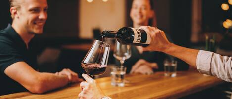 A person pouring wine into a glass at a wooden table in a dimly lit indoor setting.