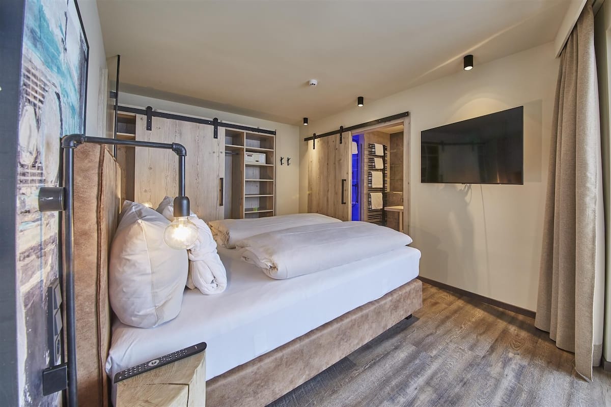 Hotelkamer met een groot bed, een bureau met lamp, een aan de muur bevestigde televisie en een kledingkast met spiegel.