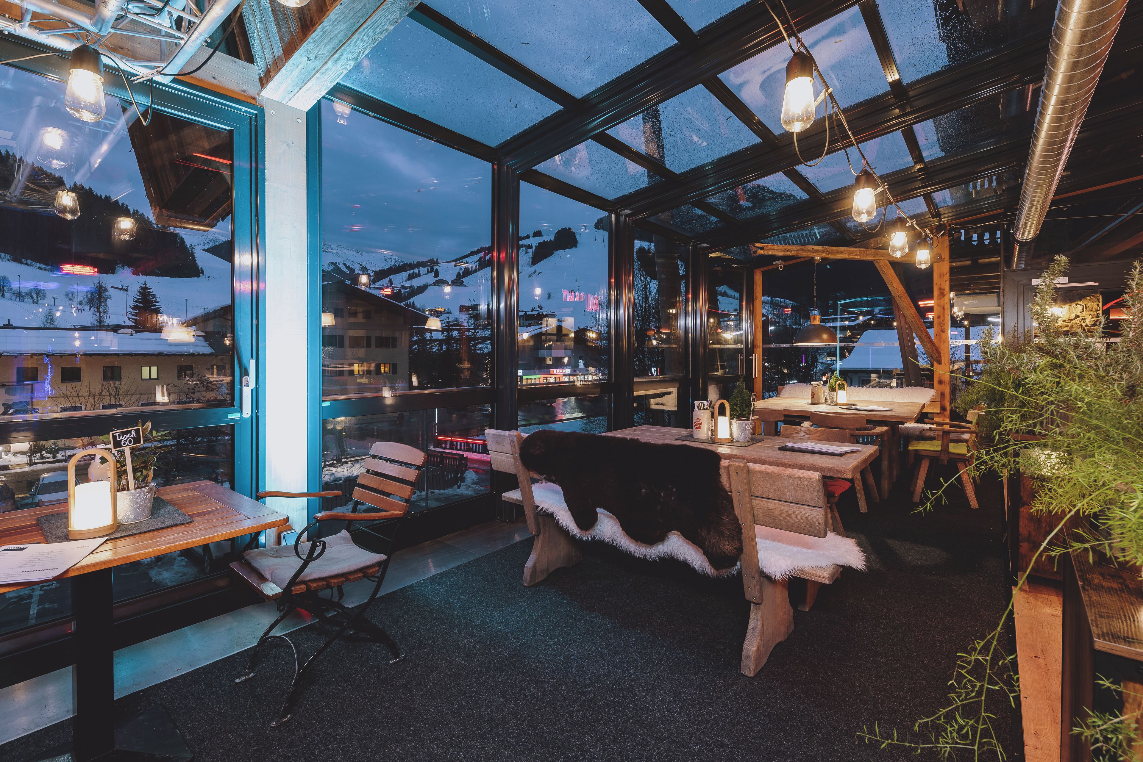 Een gezellig restaurant met houten meubels, een glazen uitbouw en uitzicht op een besneeuwde berg.