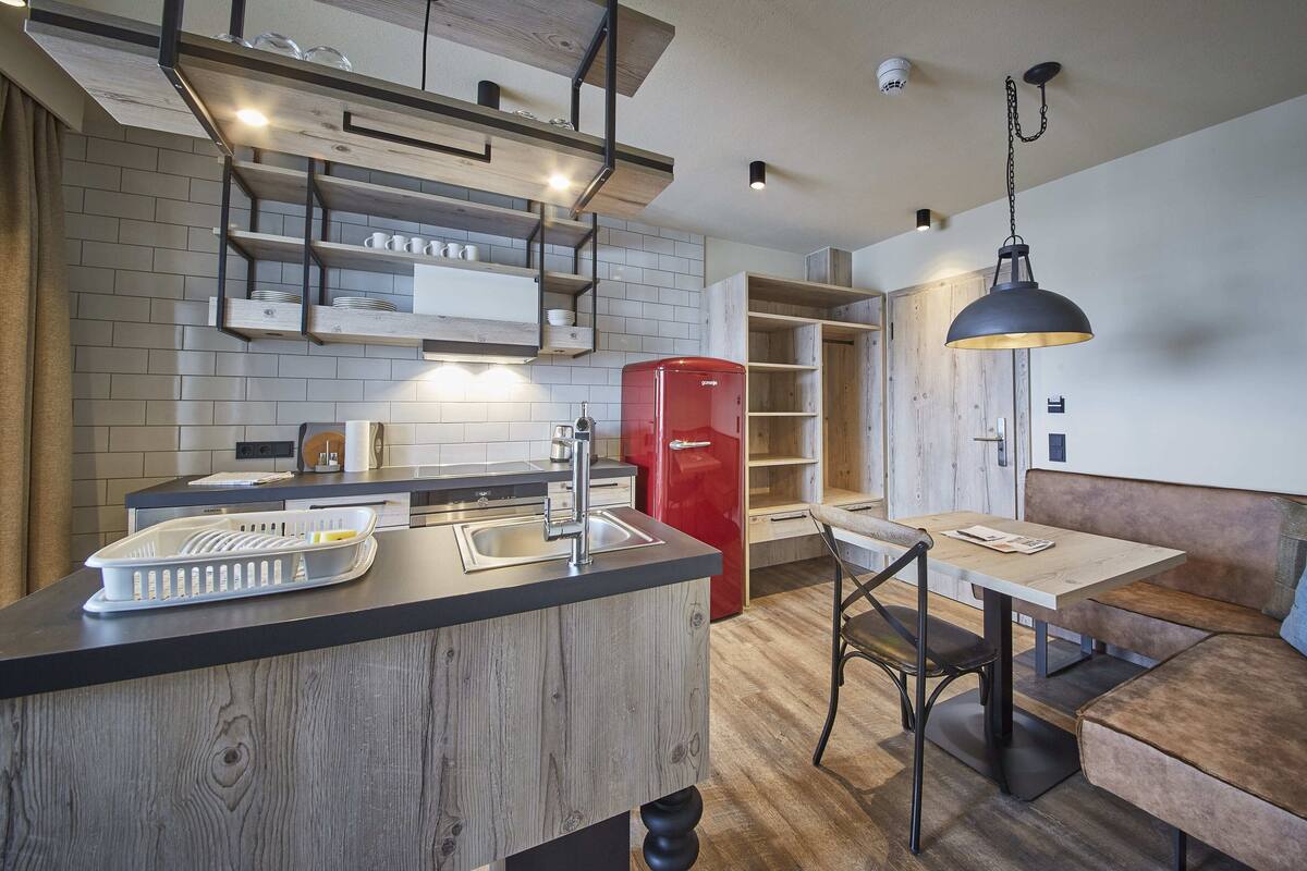 Een moderne keuken met een centraal eiland, een rode koelkast en een eethoek met een houten tafel en bank.