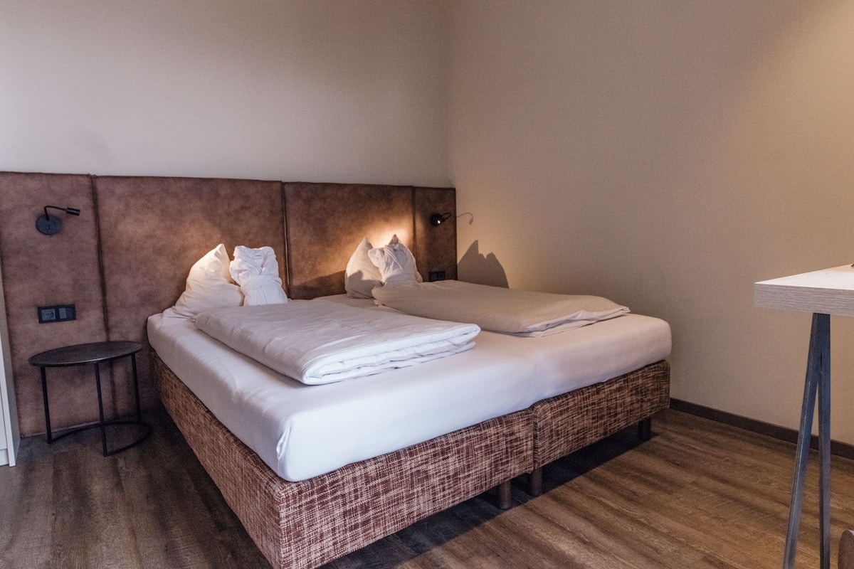 Een hotelkamer met een groot bed, een klein nachtkastje en een wandlamp.