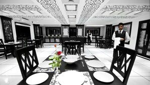 Un restaurante con decoración en blanco y negro, incluyendo techo y paredes con diseños, y un camarero de pie junto a la mesa.