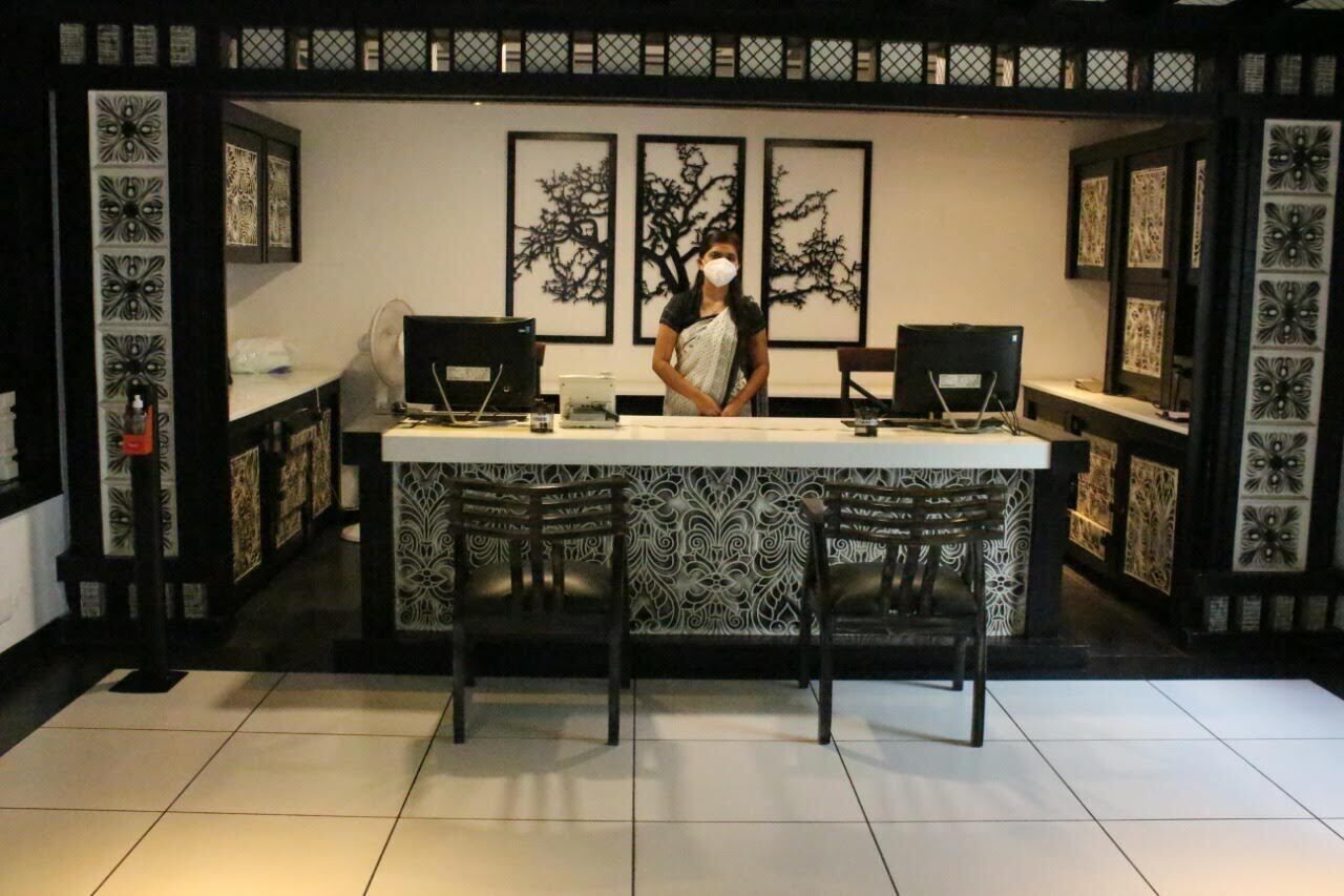 A reception desk with two computer monitors, a laptop, and a person standing behind it. There are three framed artworks on the wall behind the desk.