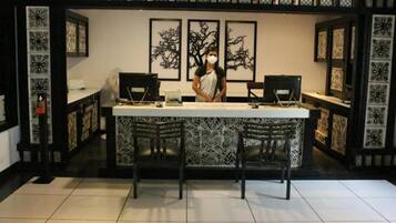 A reception desk with two computer monitors, a laptop, and a person standing behind it. There are three framed artworks on the wall behind the desk.