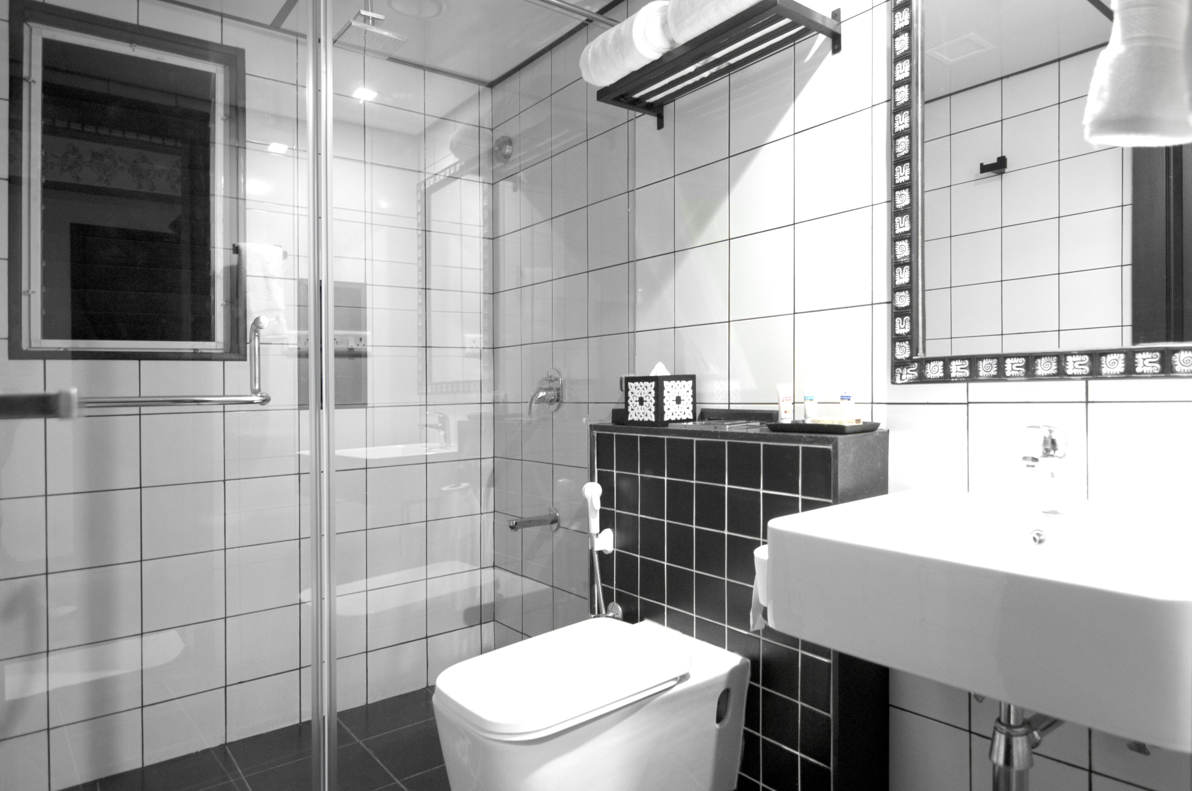 A modern bathroom with a glass shower enclosure, a white sink, and a black tiled backsplash.