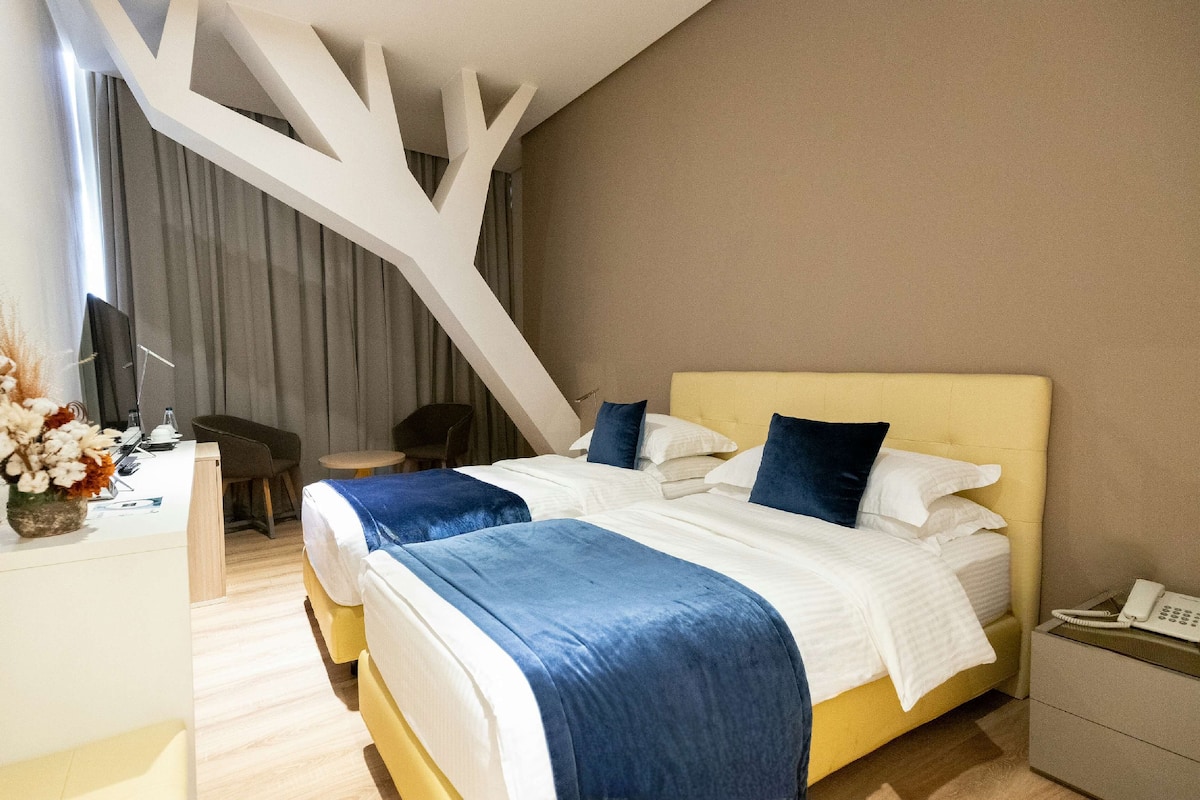 A modern hotel room with a large bed, a desk, and a chair.