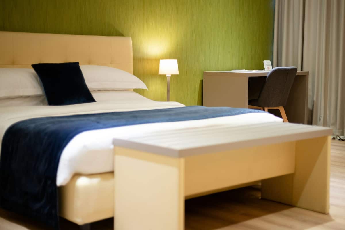 A hotel room with a bed, bedside table, desk, and chair.