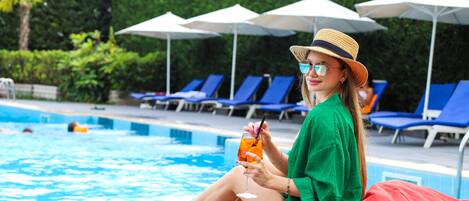 A person sitting by a pool with lounge chairs and umbrellas in the background.