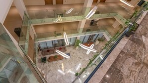 Un atrium à plusieurs niveaux avec des rampes en verre, un espace de détente central doté de canapés et des luminaires suspendus.