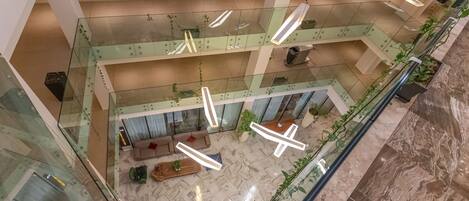 A multi-level atrium with glass railings, a central seating area with sofas, and hanging pendant lights.