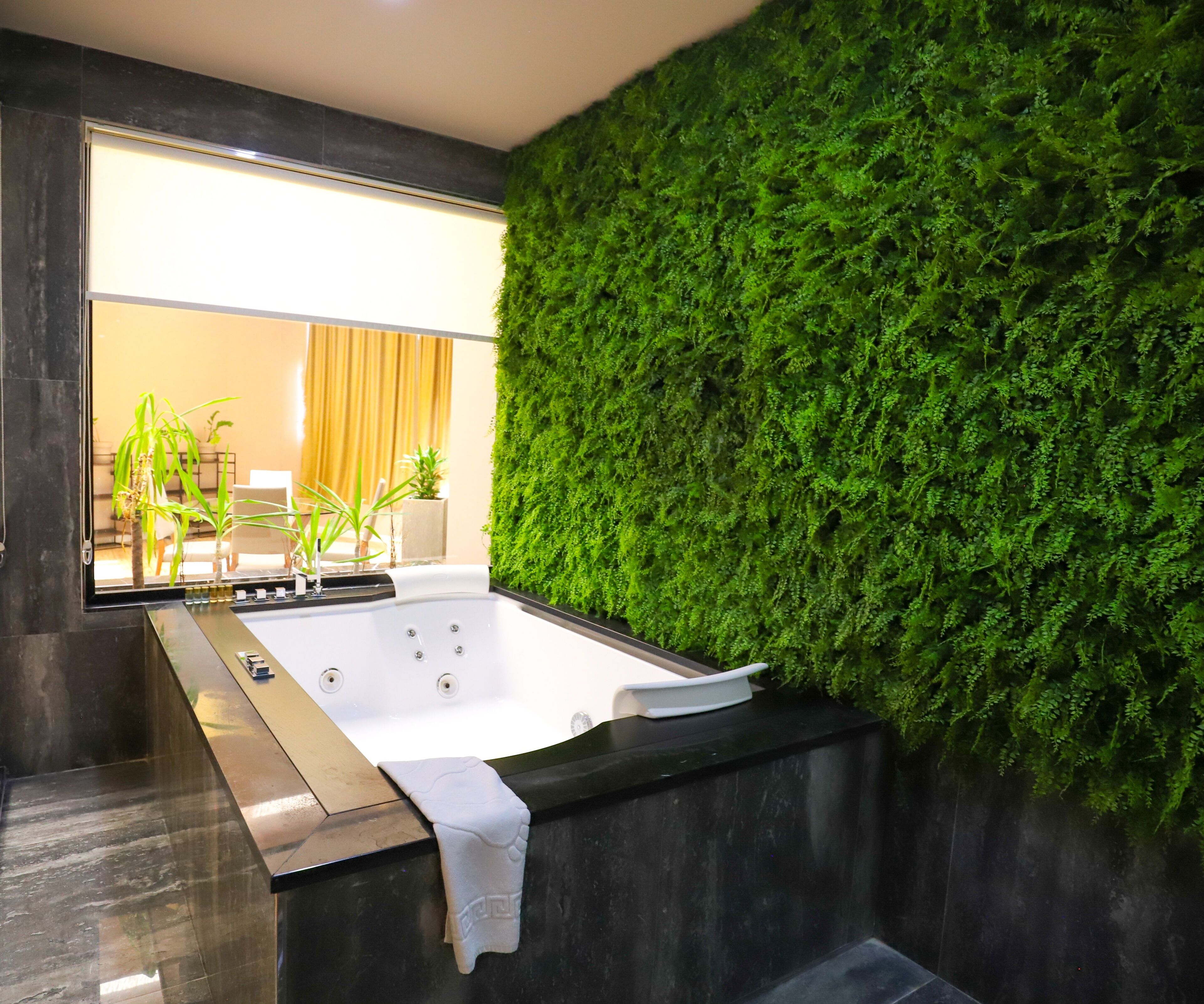 Un baño moderno con una bañera grande, una pared cubierta de musgo verde y vistas a un comedor.