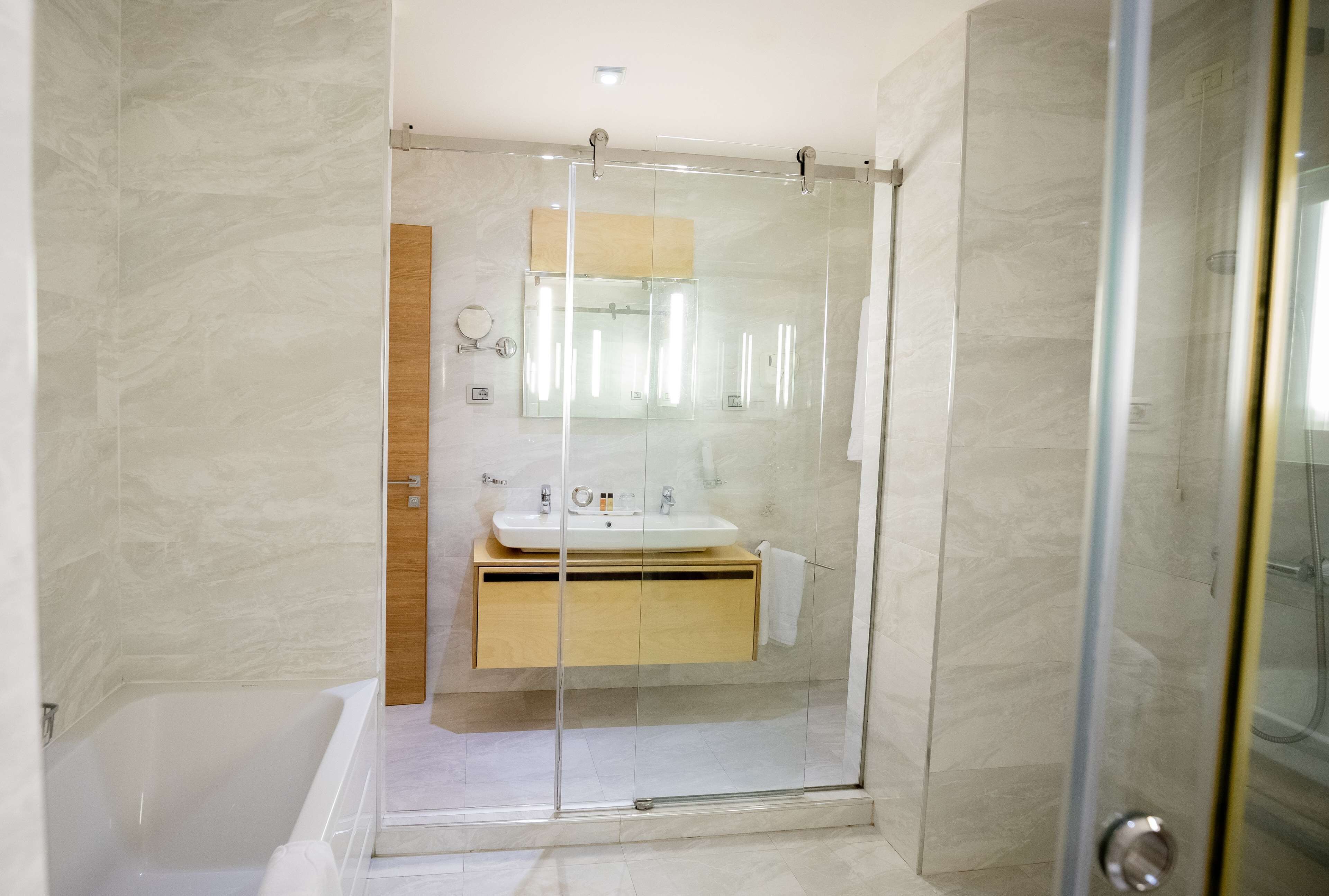 Un baño moderno con ducha compartimentada por vidrio, tocador de madera y lavamanos blanco.