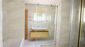 Un baño moderno con ducha compartimentada por vidrio, tocador de madera y lavamanos blanco.