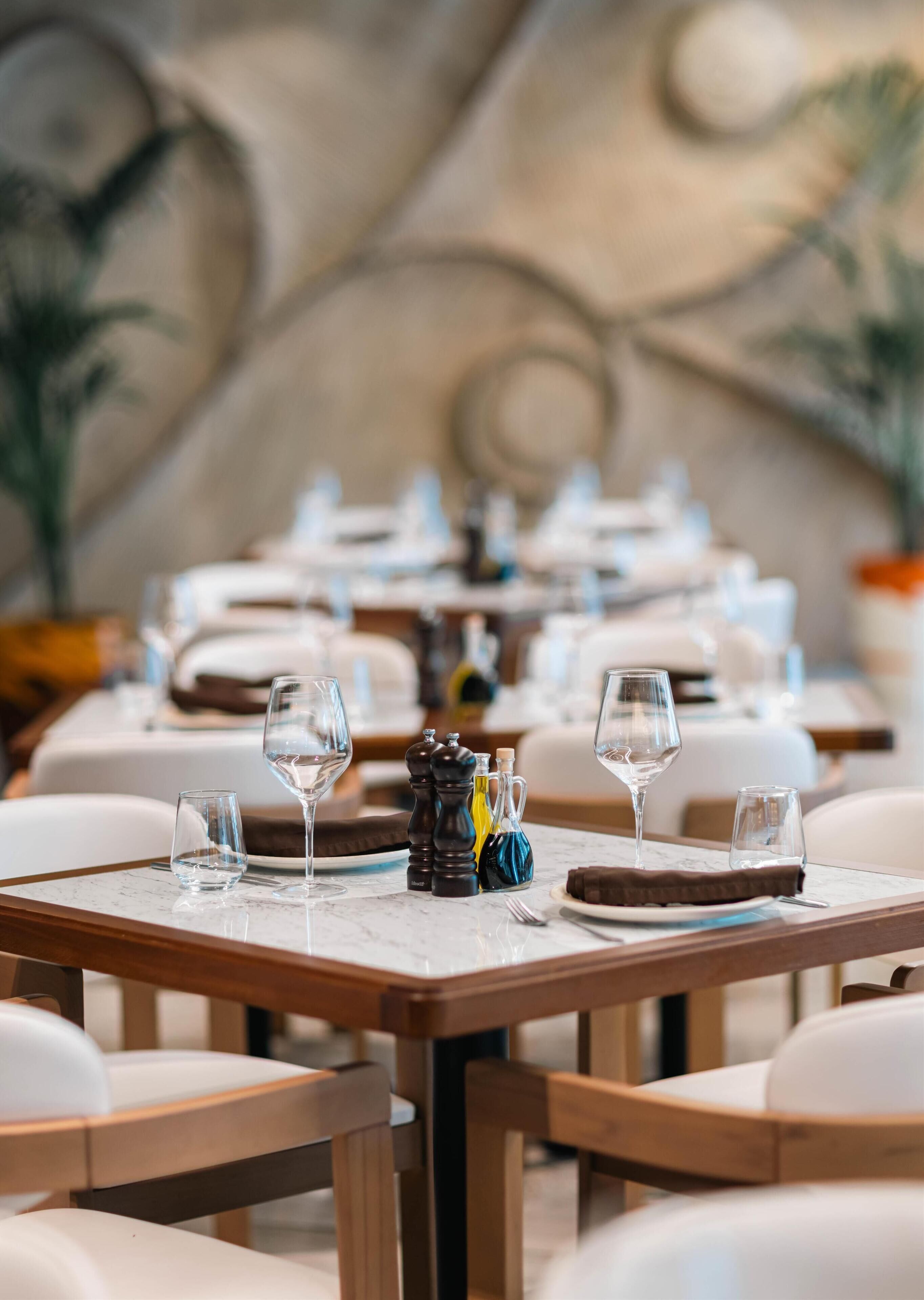A restaurant with round tables set with wine glasses and plates, and salt and pepper shakers.