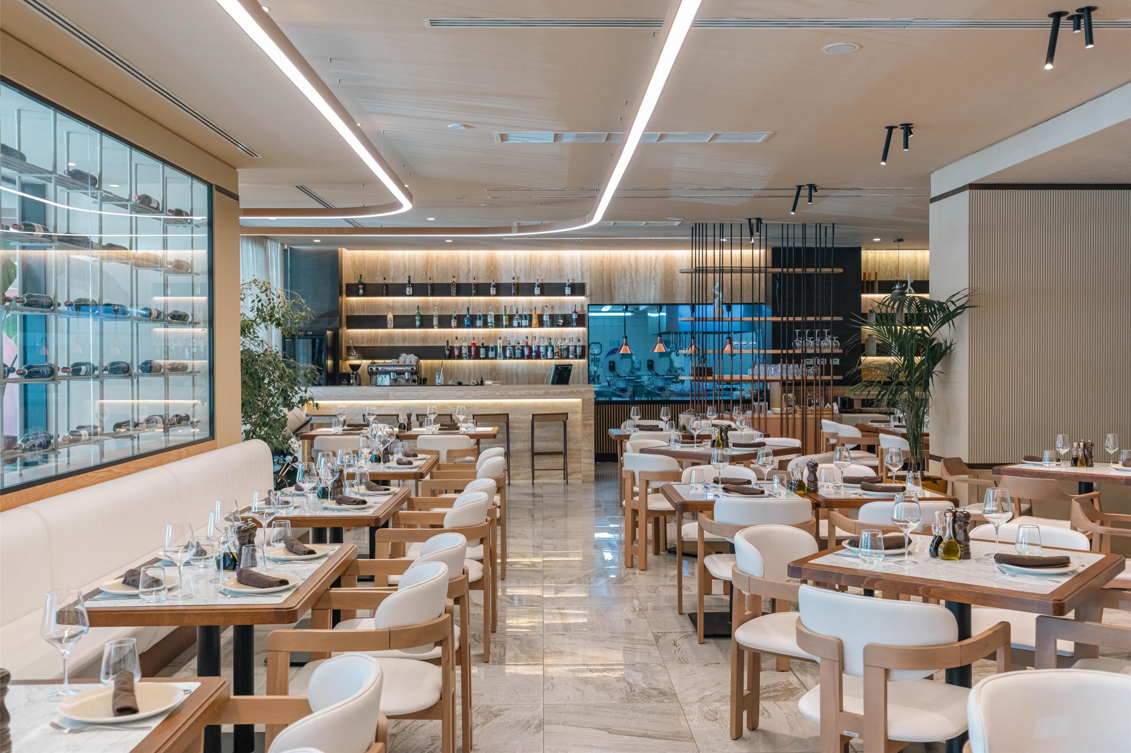 Un restaurante moderno con mesas y sillas de madera, una zona de bar y una exhibición de botellas de vino.