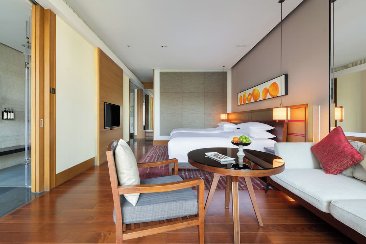 A hotel room with a bed, a sofa, a dining table, and a TV.