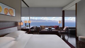 A hotel room with a large bed, a seating area with a table, and a view of the sea and mountains.