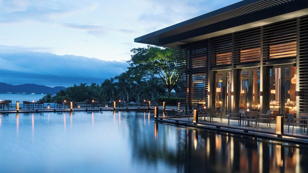 A modern resort with a serene pool, wooden deck seating, and a view of the ocean.