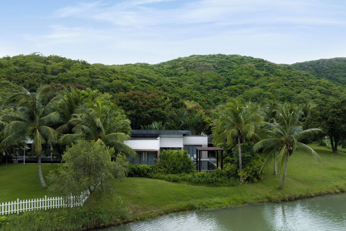 A modern house with a flat roof, surrounded by lush greenery and a river.