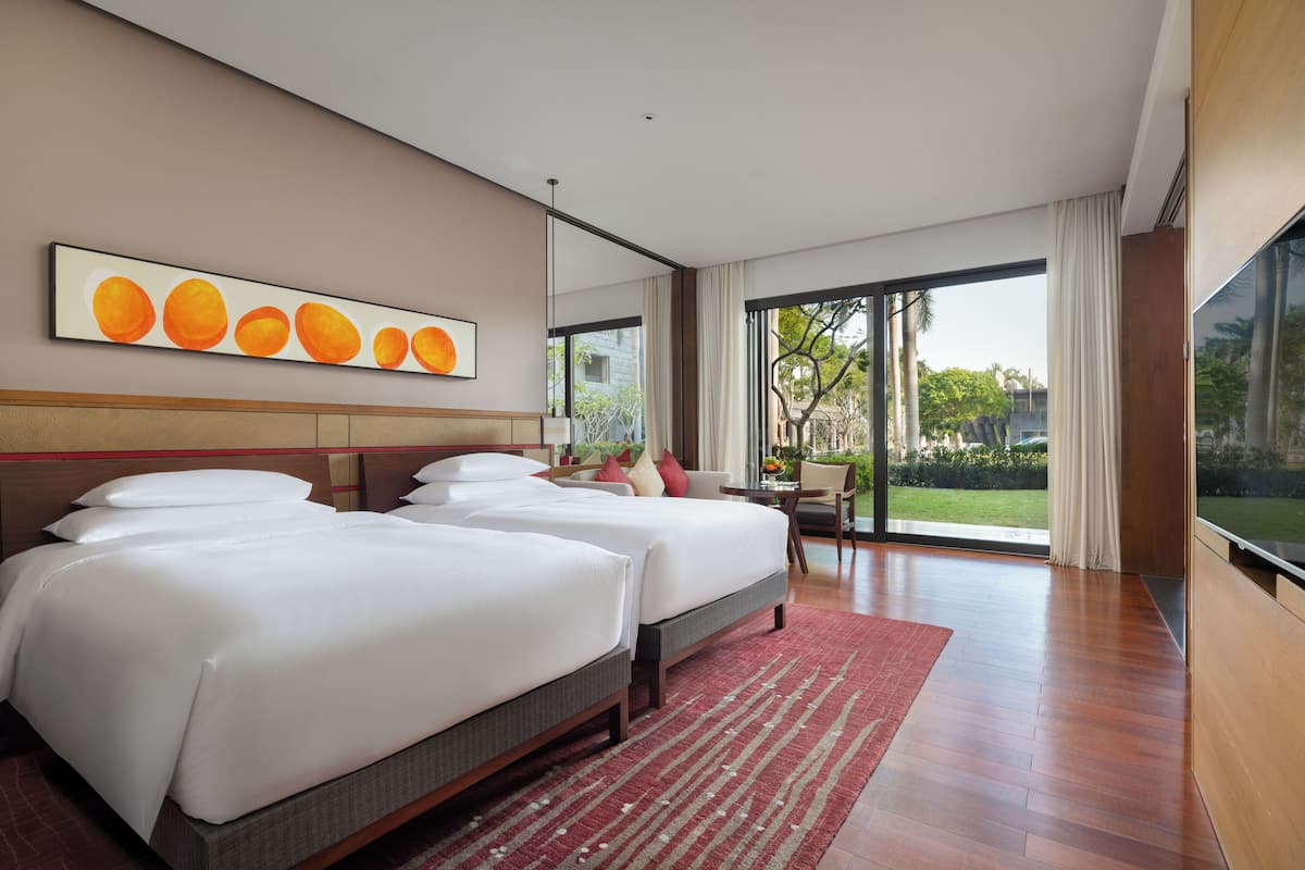A hotel room with two beds, a large window, and a view of the outdoors.